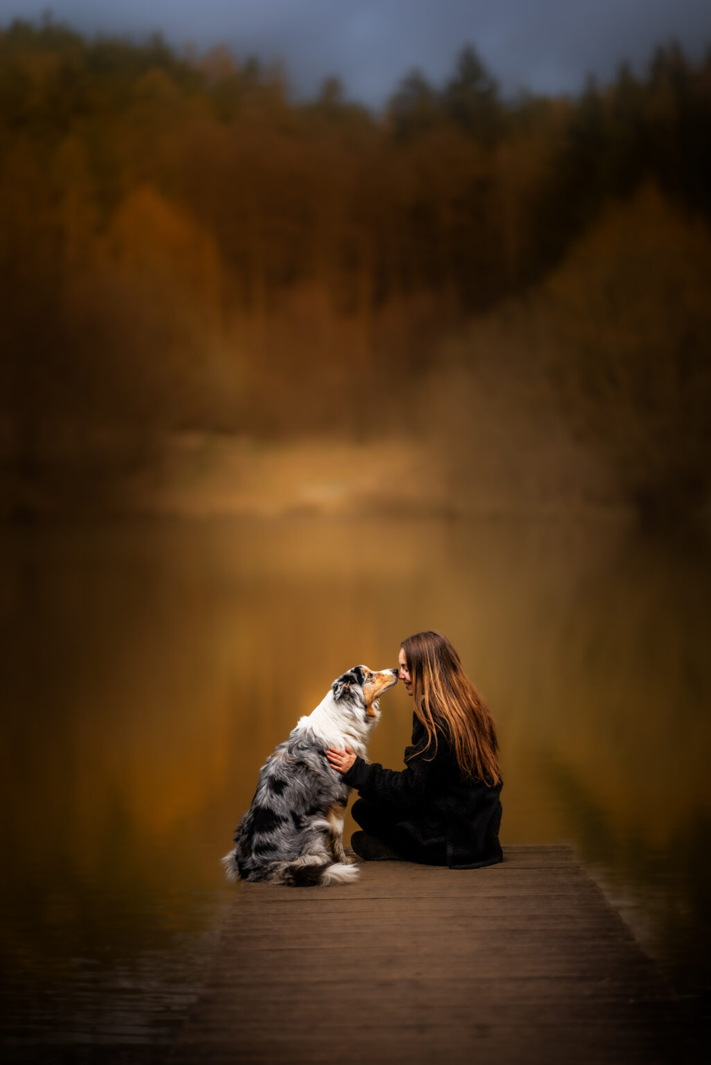Australian Shepherd und Besitzerin kuschelnd an Steg